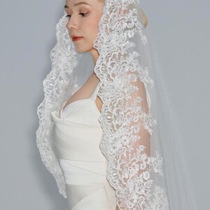 May include: A white bridal veil with a delicate lace trim. The veil is made of soft tulle and features a floral pattern.