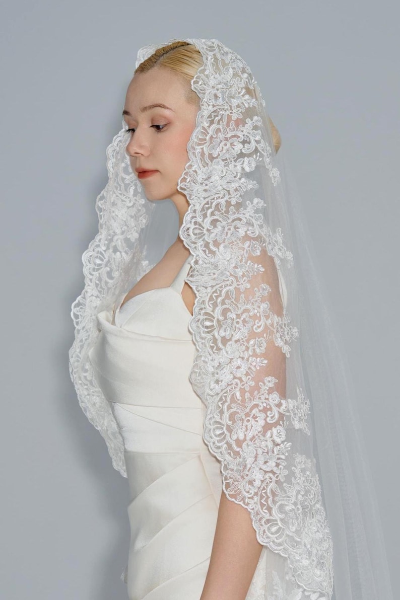 May include: A white bridal veil with a delicate lace trim. The veil is made of soft tulle and features a floral pattern.