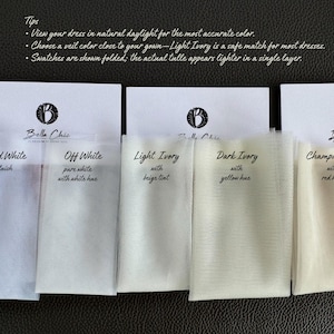 Op de afbeelding: Een selectie van tule stofstalen in verschillende tinten wit en ivoor, waaronder Cold White, Off White, Light Ivory, Dark Ivory en Champagne. Elk staal is voorzien van een kleurbeschrijving. Het Bella Chic logo is zichtbaar.