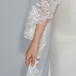 May include: A white bridal veil with a delicate lace trim. The veil is made of soft tulle and features a floral pattern.