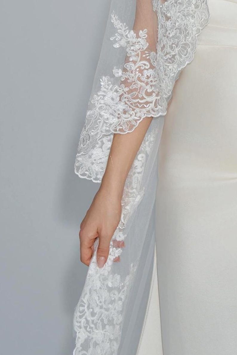 May include: A white bridal veil with a delicate lace trim. The veil is made of soft tulle and features a floral pattern.
