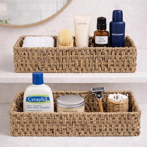 May include: Two woven rectangular storage baskets filled with toiletries. The top basket holds a white washcloth, a brush, lotion, face serum, and deodorant. The bottom basket contains Cetaphil cleanser, moisturizer, a razor, and cotton swabs.