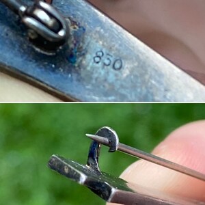May include: Close-up of a silver brooch with a pin and clasp. The back of the brooch is marked with the number "850".