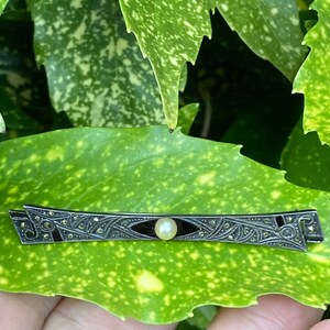 May include: A silver and black Art Deco brooch with a single pearl in the center.