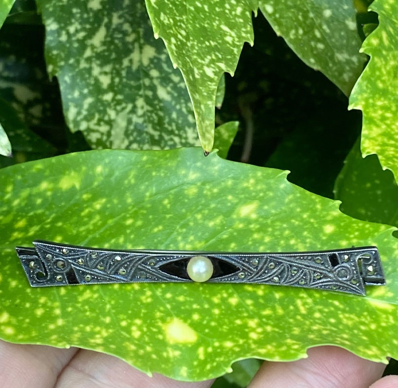 May include: A silver and black Art Deco brooch with a single pearl in the center.