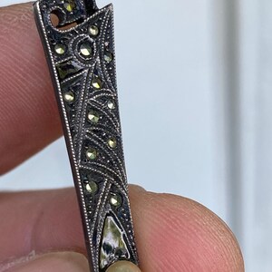 May include: A silver brooch with a geometric design and a pearl accent. The brooch is decorated with small, sparkling stones.