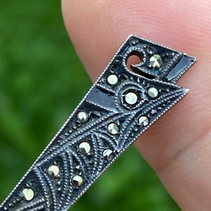 May include: A silver-toned pendant with a geometric design and black enamel accents. The pendant is decorated with small, sparkling marcasite stones.