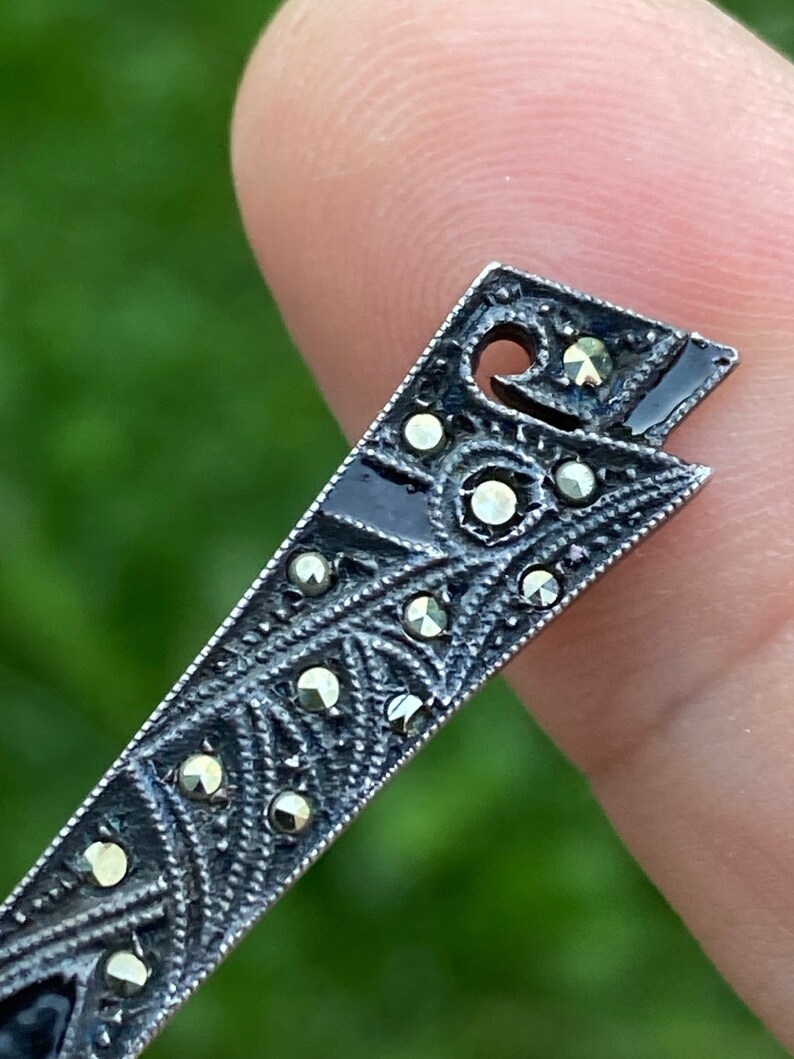May include: A silver-toned pendant with a geometric design and black enamel accents. The pendant is decorated with small, sparkling marcasite stones.