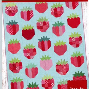 May include: A quilt pattern featuring a repeating strawberry design. The strawberries are red and pink with green tops, set against a light blue background. The pattern is titled "Strawberry Patch Quilt Pattern" and is 63" x 82".