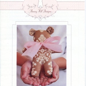 May include: A handmade baby bear doll with a brown floral pattern and pink bow. The bear's ears are a contrasting brown with a polka dot pattern. The text "Baby Bear" is at the bottom of the image.