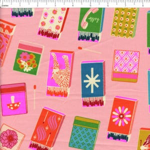 May include: Pink fabric with a repeating pattern of colorful matchboxes. The matchboxes feature various designs, including flowers, a leopard, a telephone with the word "hello", and geometric shapes. A few loose matches are scattered across the fabric.
