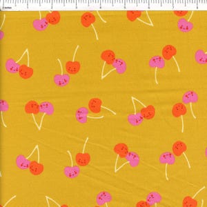 May include: Mustard yellow fabric with a repeating pattern of cartoon cherries. The cherries are in pairs, with one cherry in orange and the other in pink. Each cherry has a smiling face and white stems.