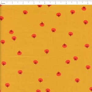 May include: A mustard yellow fabric featuring a repeating pattern of small, round, orange-red tomato icons with dark red stems. A white ruler is visible at the top edge, showing a width of approximately 8.5 inches across the fabric surface.