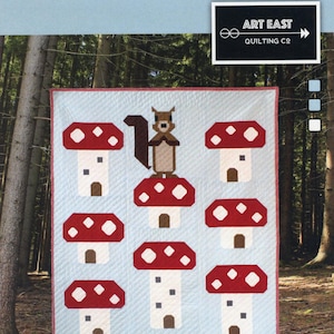May include: A quilt pattern featuring a squirrel sitting on a mushroom house. The pattern includes a total of seven mushroom houses with red and white tops and white houses. The pattern is titled "Mushroom King: A Squirrel & His Kingdom" and is a 40" x 48" quilt pattern.
