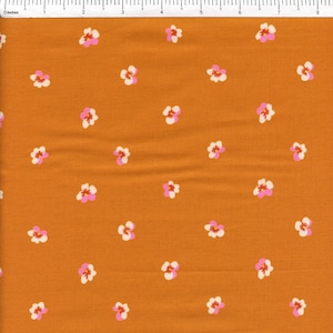 May include: Close-up of a fabric with a repeating floral pattern. The fabric has a warm orange-brown background. Small flowers with white petals, pink centers, and yellow stamens are scattered across the surface.
