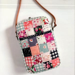 May include: A rectangular patchwork crossbody bag with a brown leather strap. The bag is made of various fabric squares in floral, gingham, and polka dot patterns, with colors including pink, blue, and white. The bag has a metal clasp.