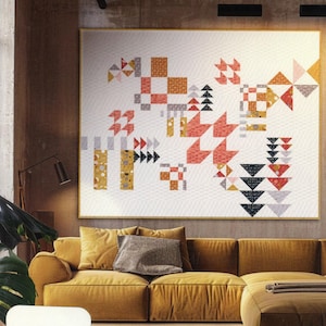 May include: A modern quilt pattern with geometric shapes in shades of red, orange, yellow, gray, and black. The quilt is hanging on a wall in a room with a brown leather sofa and a rug. The quilt is titled "Zen Chic Breeze" by Brigitte Heitland.