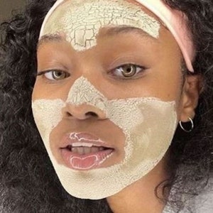 May include: A person with dark curly hair is wearing a light pink headband and a light green face mask that is cracking. The mask is covering the person's forehead, nose, and chin.