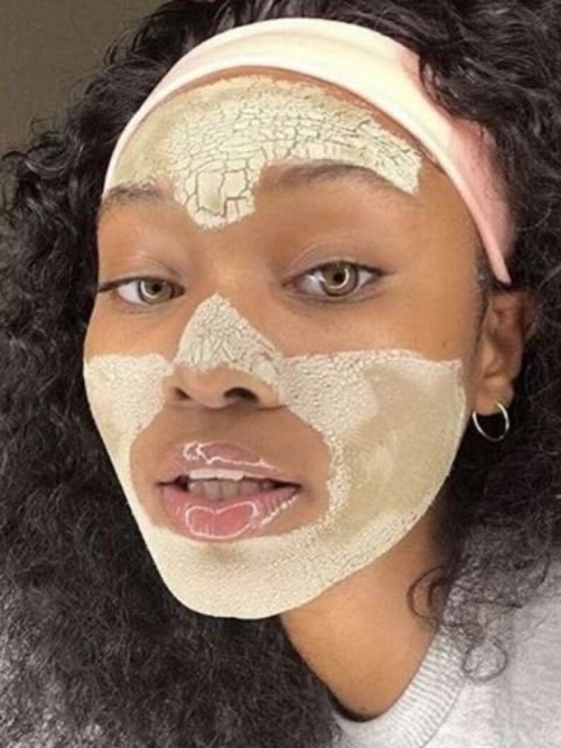 May include: A person with dark curly hair is wearing a light pink headband and a light green face mask that is cracking. The mask is covering the person's forehead, nose, and chin.