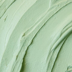 May include: Close-up of a smooth, green face mask with a swirling, textured pattern. The mask has a creamy consistency and appears to be made from natural ingredients.