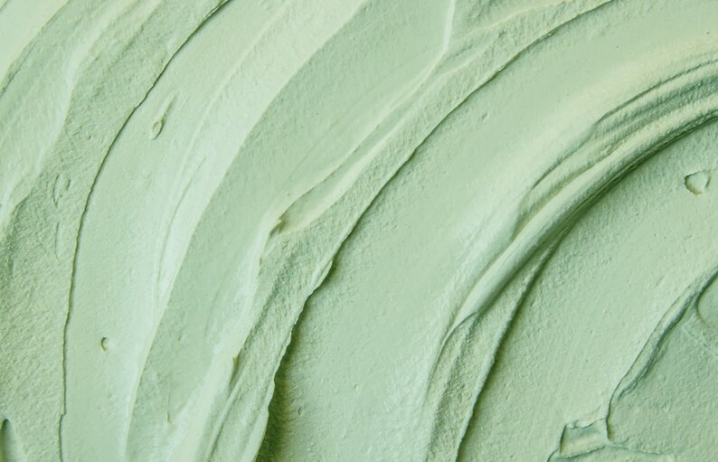 May include: Close-up of a smooth, green face mask with a swirling, textured pattern. The mask has a creamy consistency and appears to be made from natural ingredients.