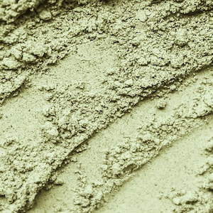 May include: Close-up of a green powder with a rough, textured surface. The powder is arranged in diagonal lines, creating a visually interesting pattern.