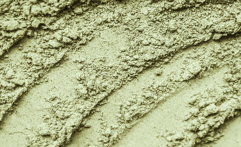 May include: Close-up of a green powder with a rough, textured surface. The powder is arranged in diagonal lines, creating a visually interesting pattern.