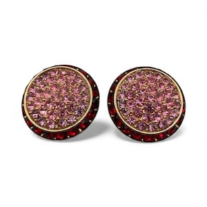 May include: A pair of round stud earrings. Each earring features a gold-tone setting, a center of pink crystals, and a border of red crystals. The earrings are set against a white background.