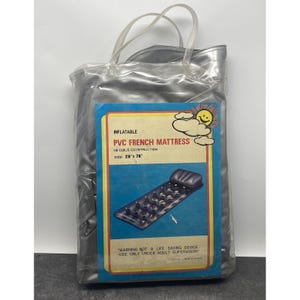Op de afbeelding: Een zilverkleurige, doorzichtige plastic zak met een opblaasbare PVC Franse matras. De blauwe matras meet 71 x 198 cm. De verpakking bevat de tekst "PVC French Mattress" en "Warning-Not a Life Saving Device - Use Only Under Adult Supervision."