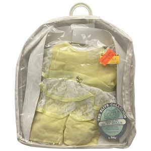 Op de afbeelding: Een gele poppenoutfit met kanten rand, verpakt in een doorzichtige plastic hoes met een handvat. De outfit bevat een jurk en een korte broek. De verpakking is gelabeld met "The Elite Collection" en "Made to Fit 38-43 cm Dolls."