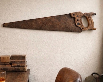 May include: A vintage hand saw with a wooden handle and a rusty blade is mounted on a textured wall. The saw is a dark brown color and has a classic design. The handle has decorative carvings.