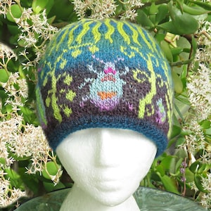 May include: A colorful knit beanie with a whimsical design. The hat features a blue base with a central insect motif in light blue, orange, and purple. Green and yellow patterns adorn the top, with a dark blue brim. The hat is displayed on a white mannequin head.