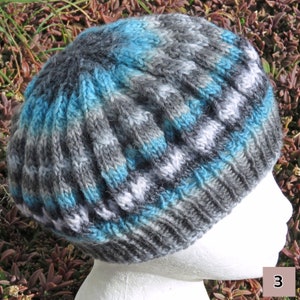 May include: A gray, blue, and white knitted beanie with a textured pattern. The beanie is on a white mannequin head.