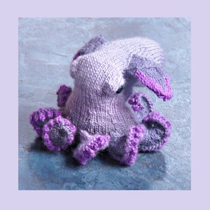 Puede incluir: Un juguete de peluche de pulpo de punto morado y lavanda con una superficie texturizada. El pulpo tiene ocho tentáculos con ribete morado.