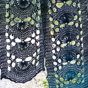 Könnte beinhalten: Nahaufnahme eines blauen und türkisfarbenen gestrickten Schals mit einem Spitzenmuster. Der Schal ist aus feinem Garn gefertigt und hat ein zartes, luftiges Gefühl.
