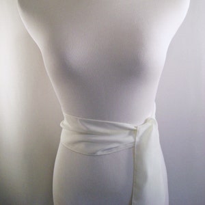 May include: A white, ribbed, fabric mannequin with a white fabric sash tied around the waist.