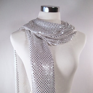 May include: A white sequined scarf with silver sequins. The scarf is draped over a white mannequin.