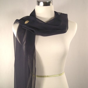 May include: A black sheer scarf with a gold pin. The scarf is draped around a white mannequin.