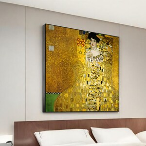 Op de afbeelding: Een schilderij van een vrouw in een gouden jurk met een geometrisch patroon. De achtergrond is ook goudkleurig met een geometrisch patroon. De vrouw draagt een ketting en heeft donker haar.