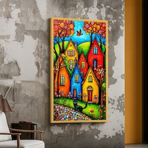 Puede incluir: Una pintura enmarcada representa una escena de un pueblo vibrante. Casas coloridas en tonos amarillos, naranjas, azules y rojos se encuentran entre árboles con follaje otoñal. Un gato negro está sentado en un camino empedrado y un pájaro vuela en el cielo.