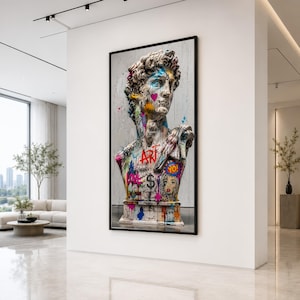 Puede incluir: Una impresión de arte mural vertical enmarcada que presenta un busto de mármol clásico de David cubierto con grafitis vibrantes. La escultura muestra salpicaduras de pintura coloridas, un corazón rosa, un signo de dólar y el texto ART y YO.