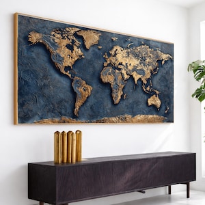May include: A large, rectangular wall art piece featuring a world map. The map is rendered in gold against a textured, dark blue background, framed in a gold-toned wood. The continents are raised, creating a 3D effect. The artwork is mounted above a dark wood cabinet.