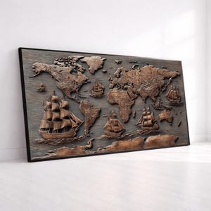 Op de afbeelding: Een houten wereldkaart met een donkerbruine afwerking, zwart omlijst. De kaart toont continenten en oceanen in reliëf, met gebeeldhouwde zeilschepen. Het kunstwerk wordt tentoongesteld tegen een witte muur.