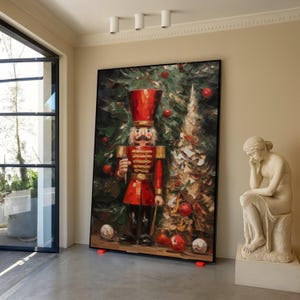 Może przedstawiać: Duże, oprawione dzieło sztuki przedstawiające szczegółowy obraz żołnierza-dziadka do orzechów w czerwonym mundurze i czapce, stojącego przed choinką. Dzieło sztuki jest podparte na czerwonych podporach w pokoju o neutralnej palecie kolorów.