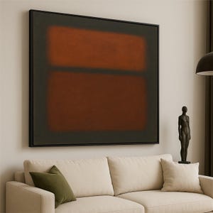 Pode incluir: Grande pintura abstrata com moldura preta. A obra apresenta duas formas retangulares castanhas sobre um fundo escuro. Um sofá bege com almofadas verdes e brancas está em primeiro plano. Decoração moderna.