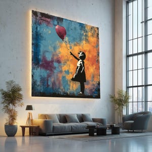 Puede incluir: Una obra de arte grande y enmarcada que representa a una niña pequeña extendiendo la mano hacia un globo rojo en forma de corazón. El fondo presenta una vibrante mezcla de pinceladas azules, naranjas y moradas. La obra está montada en una pared blanca.