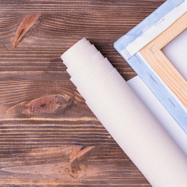 Pu&ograve; includere: Una tela bianca arrotolata con una cornice in legno e tessuto blu sui bordi. La tela &egrave; su una superficie in legno marrone.