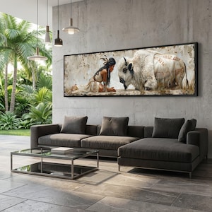 May include: A framed artwork depicts a Native American woman kneeling before a white bison. The woman wears a traditional dress and headdress. The bison has text on its side. The artwork is displayed above a dark gray sectional sofa.