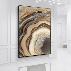 Puede incluir: Una pieza de arte mural rectangular que presenta un patrón abstracto de piedra ágata con capas concéntricas en tonos crema, beige, topo y marrón oscuro. El diseño incluye acentos de oro metálico y un centro cristalino texturizado en un marco negro.