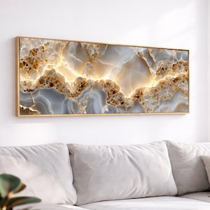 May include: A rectangular wall art piece featuring a horizontal abstract pattern of swirling grey, white, and gold tones that mimic the appearance of polished agate or marble stone, enclosed within a thin, metallic gold-colored frame.